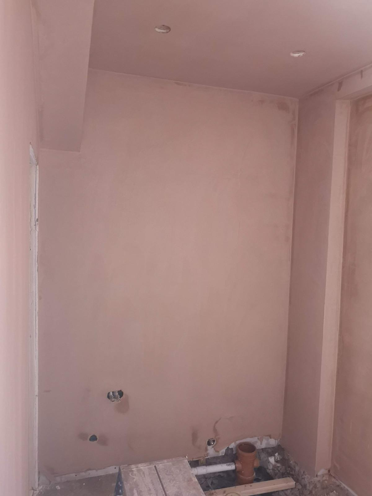 Fresh plaster on the walls and ceiling of a small room with exposed plumbing at floor level