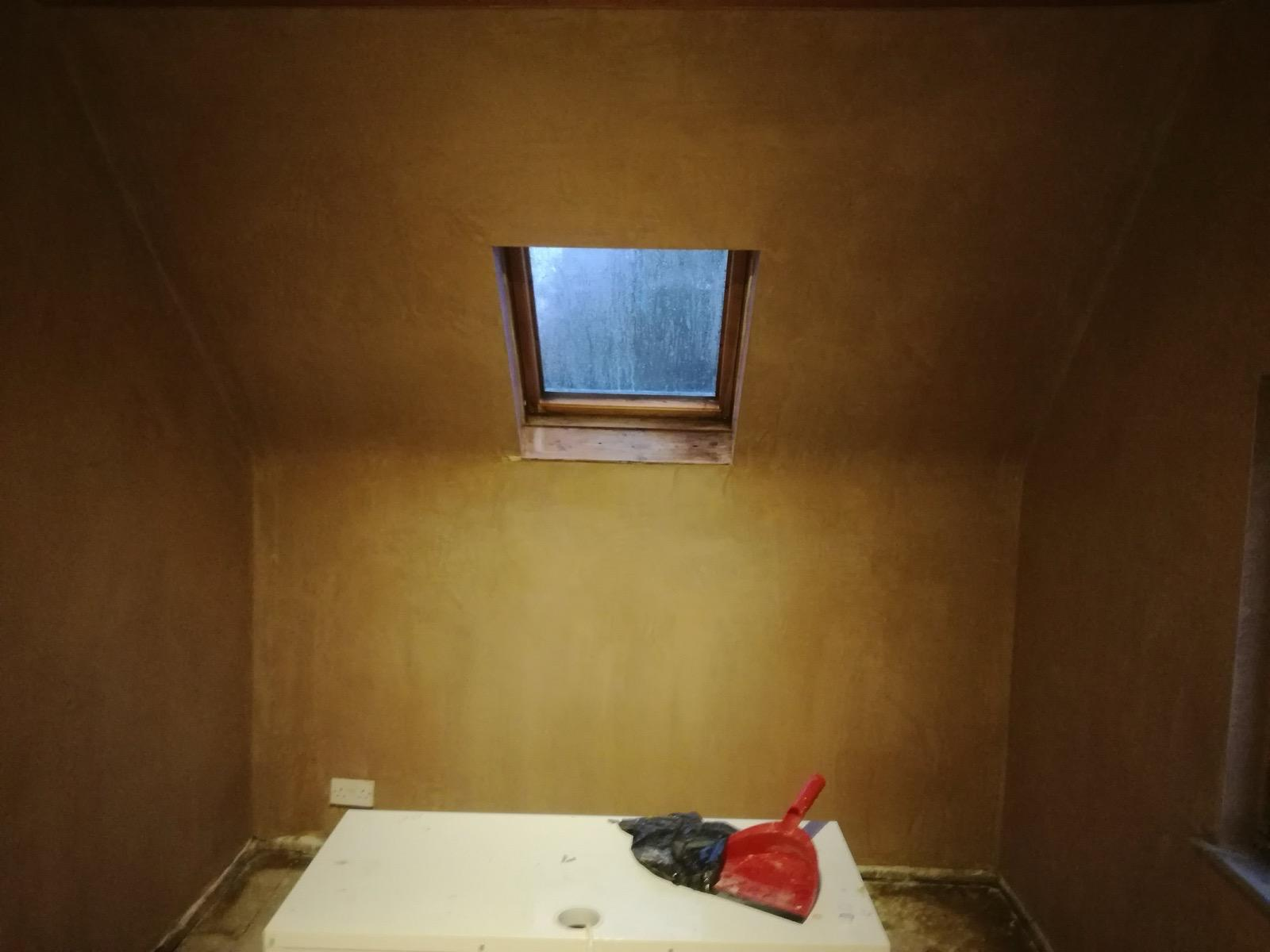 Freshly plastered wall and sloping ceiling around a roof window, with a table and tools below