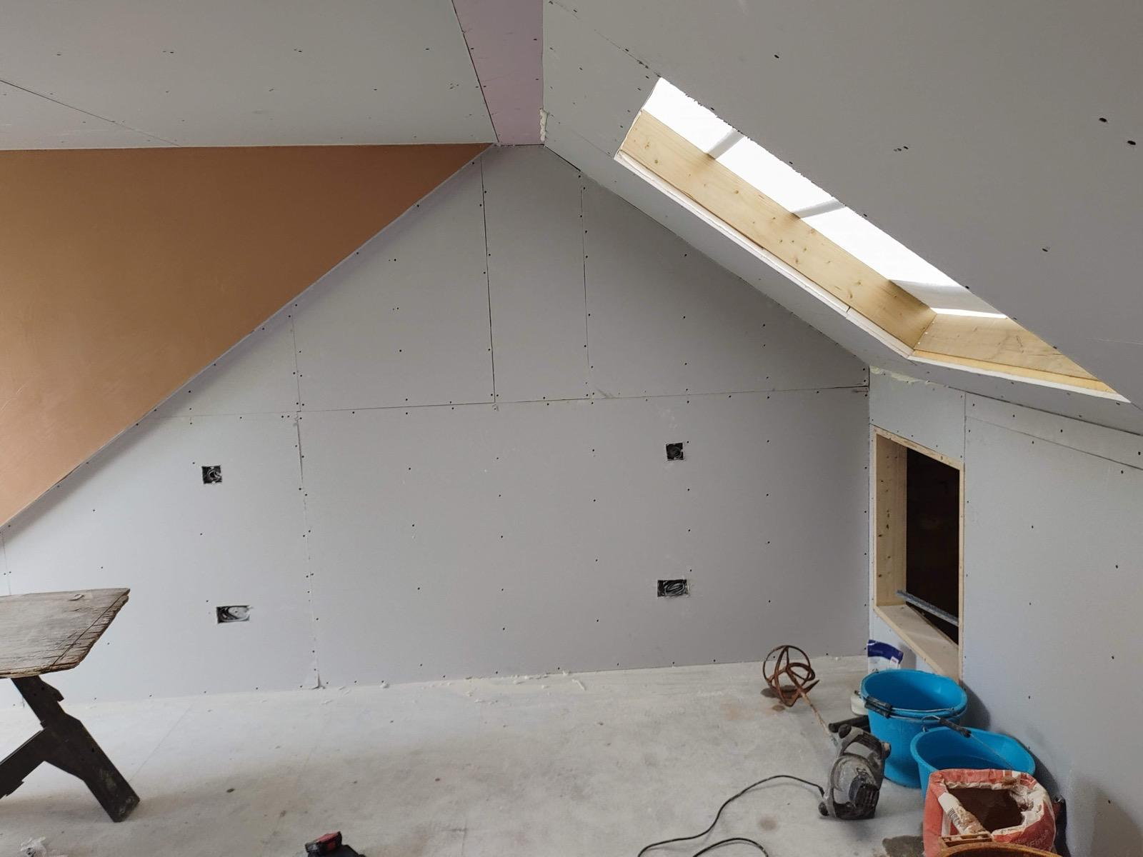 Plasterboarded loft gable wall beside a roof window, prepared for plastering