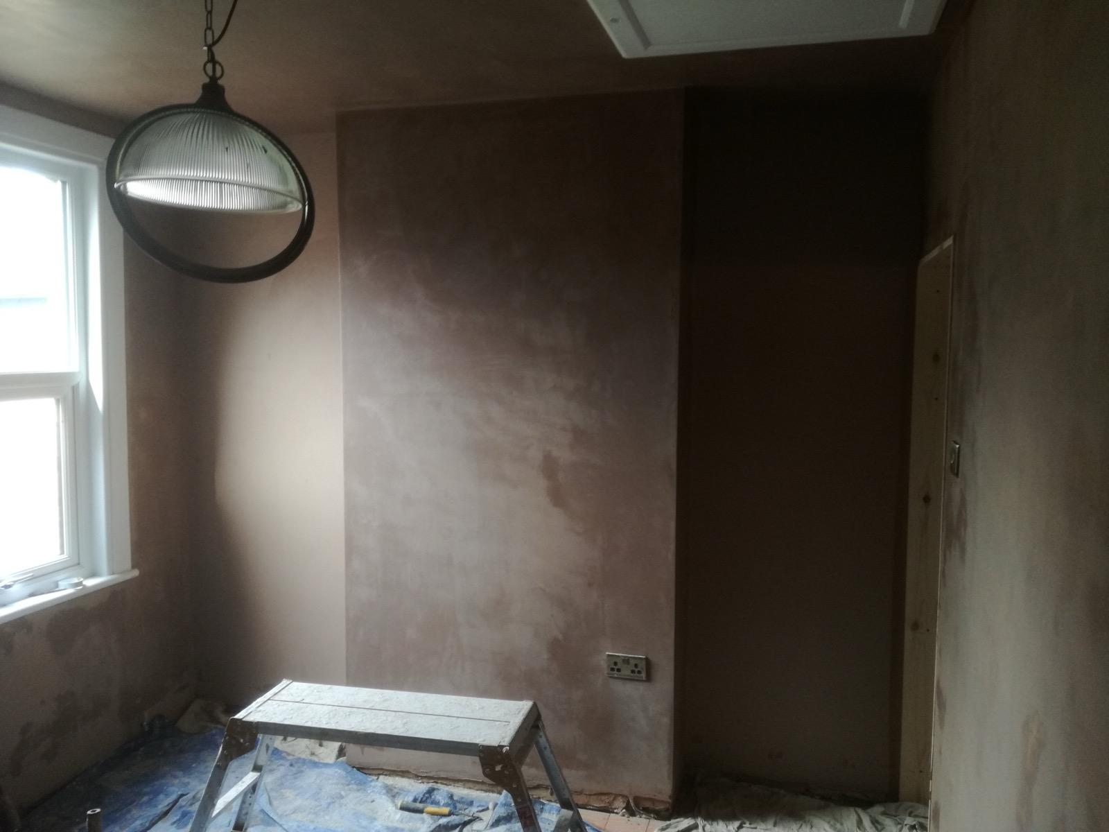 Fresh plaster on a room wall beside a window and hanging light, with floor protection in place