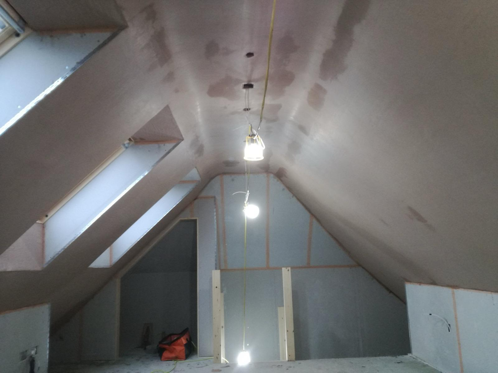 Pitched loft ceiling showing fresh plaster around roof windows and temporary lights