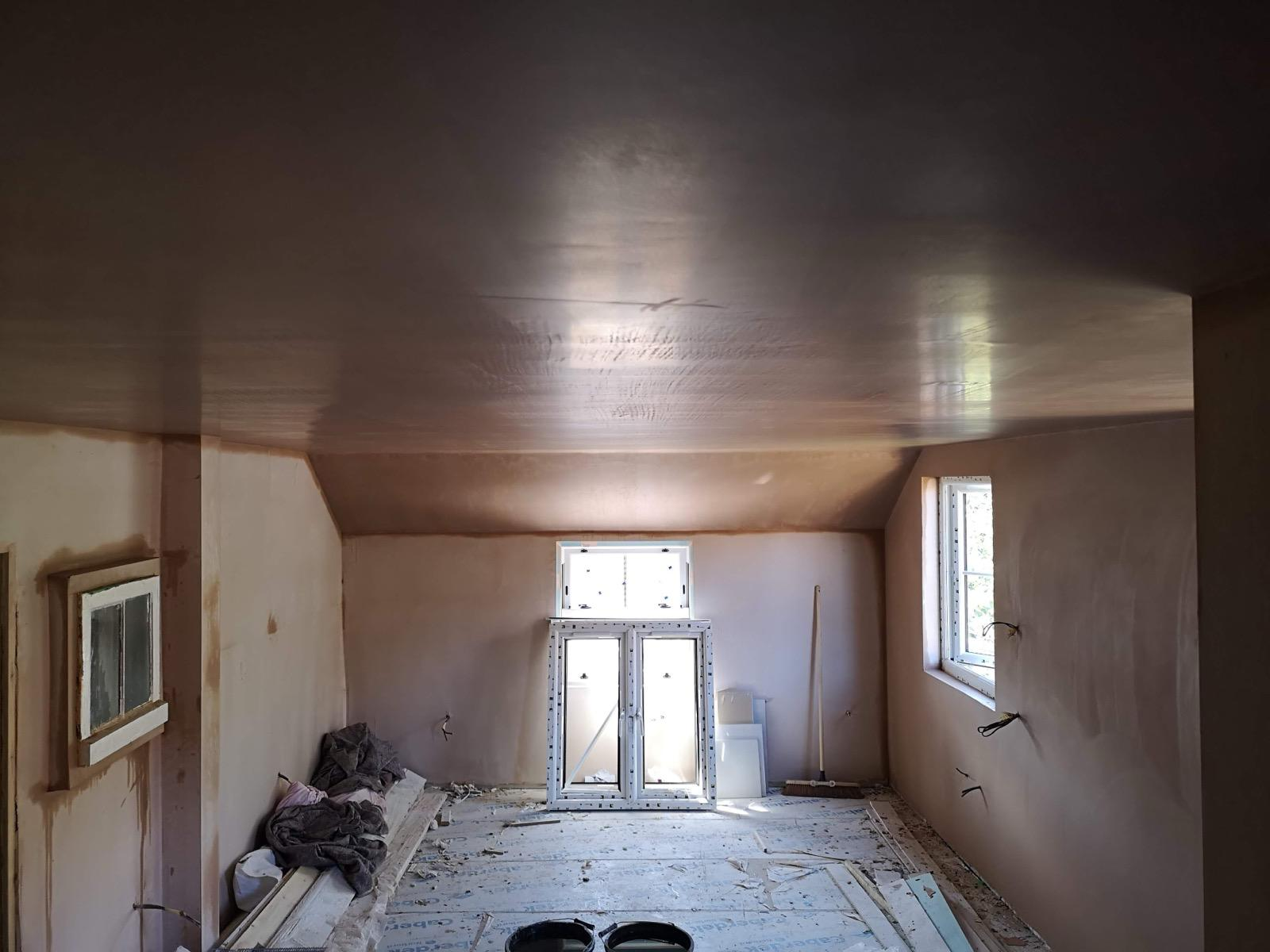 Wide room with freshly plastered walls and ceiling, and protected floor beneath