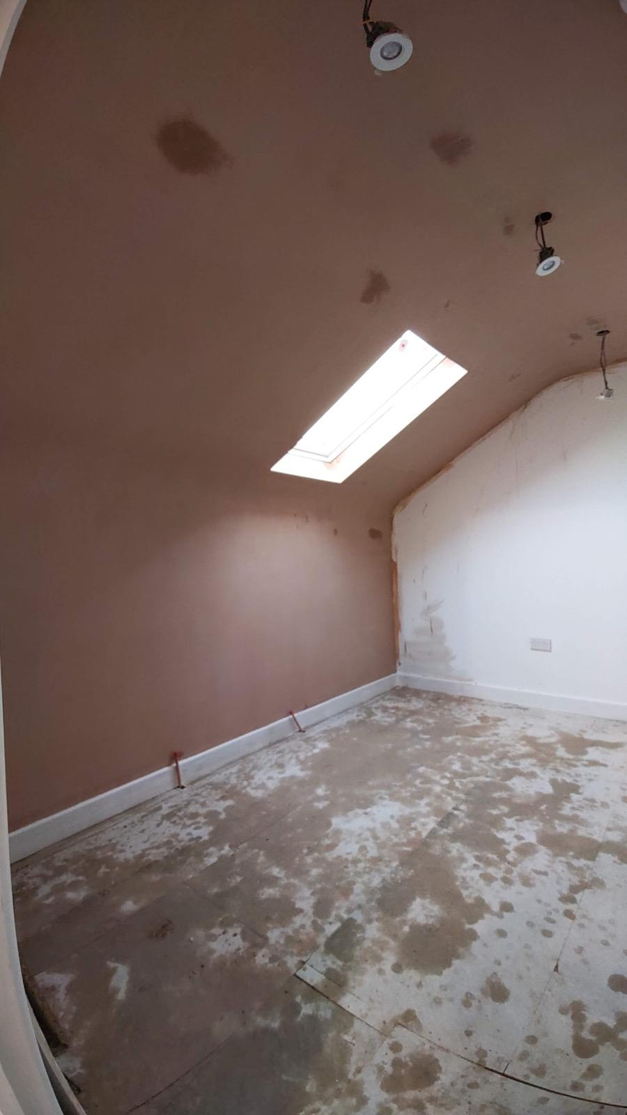 Newly plastered sloped attic ceiling with a roof window and spotlights