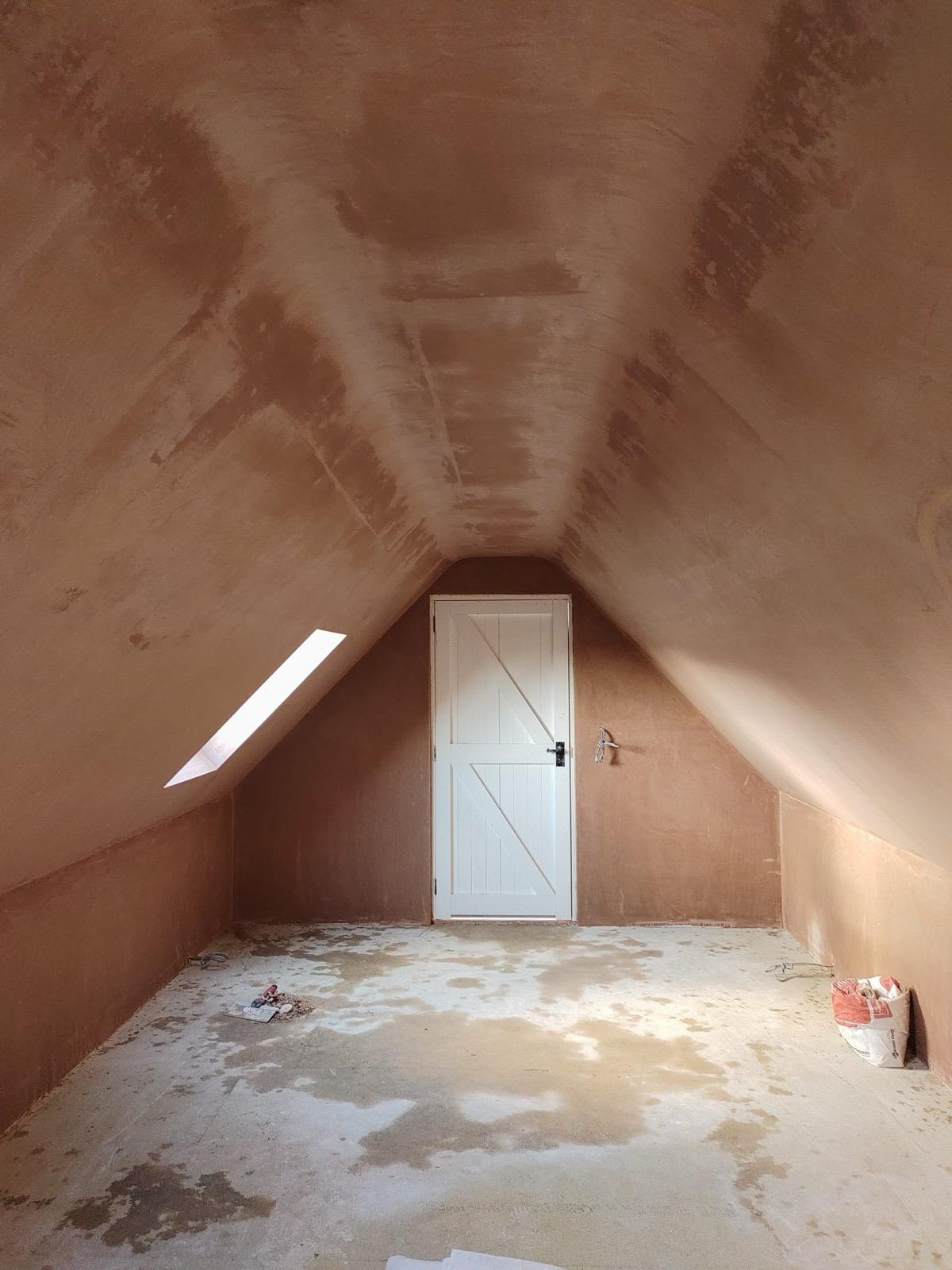 Fresh plaster across sloping loft ceiling and end wall around a door