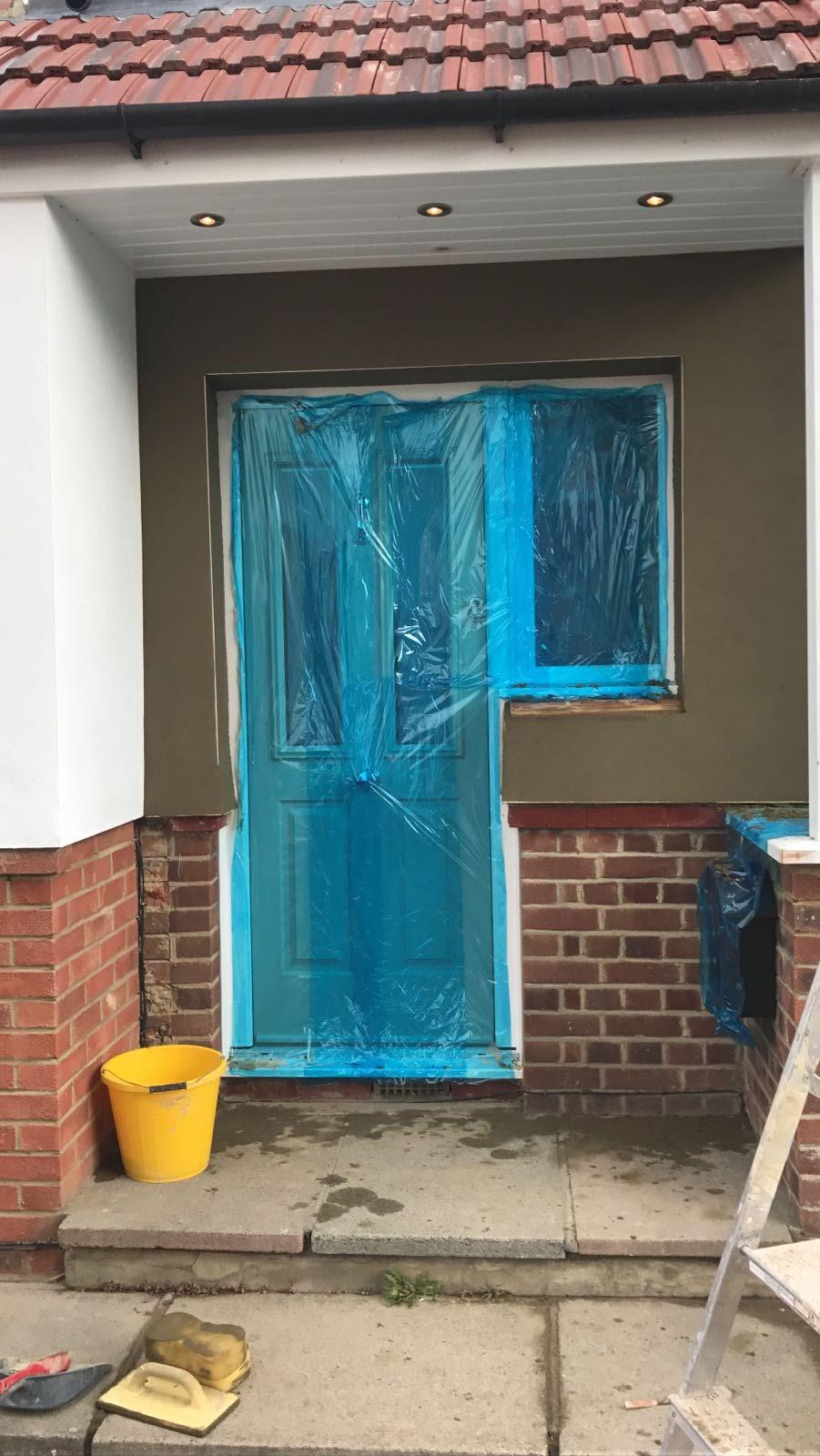 Fresh dark render around a covered front entrance, with door and window protected by blue sheeting