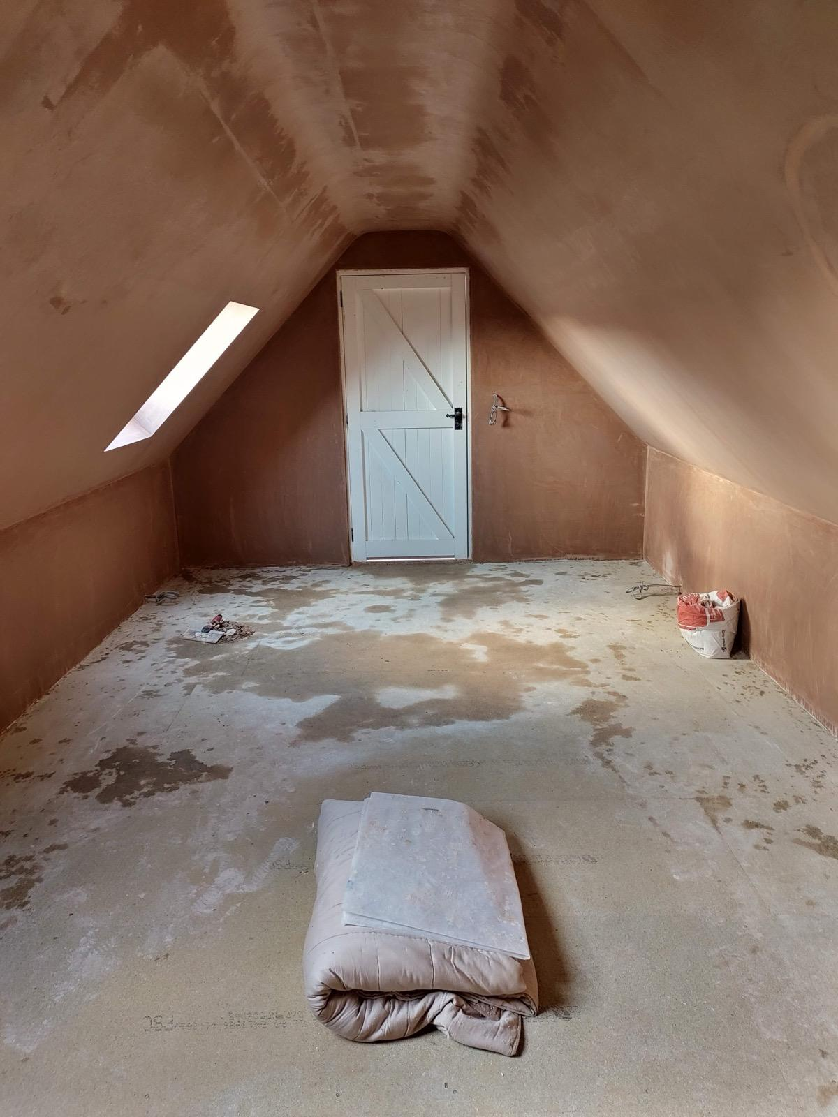 Freshly plastered loft with white ledged door and roof window