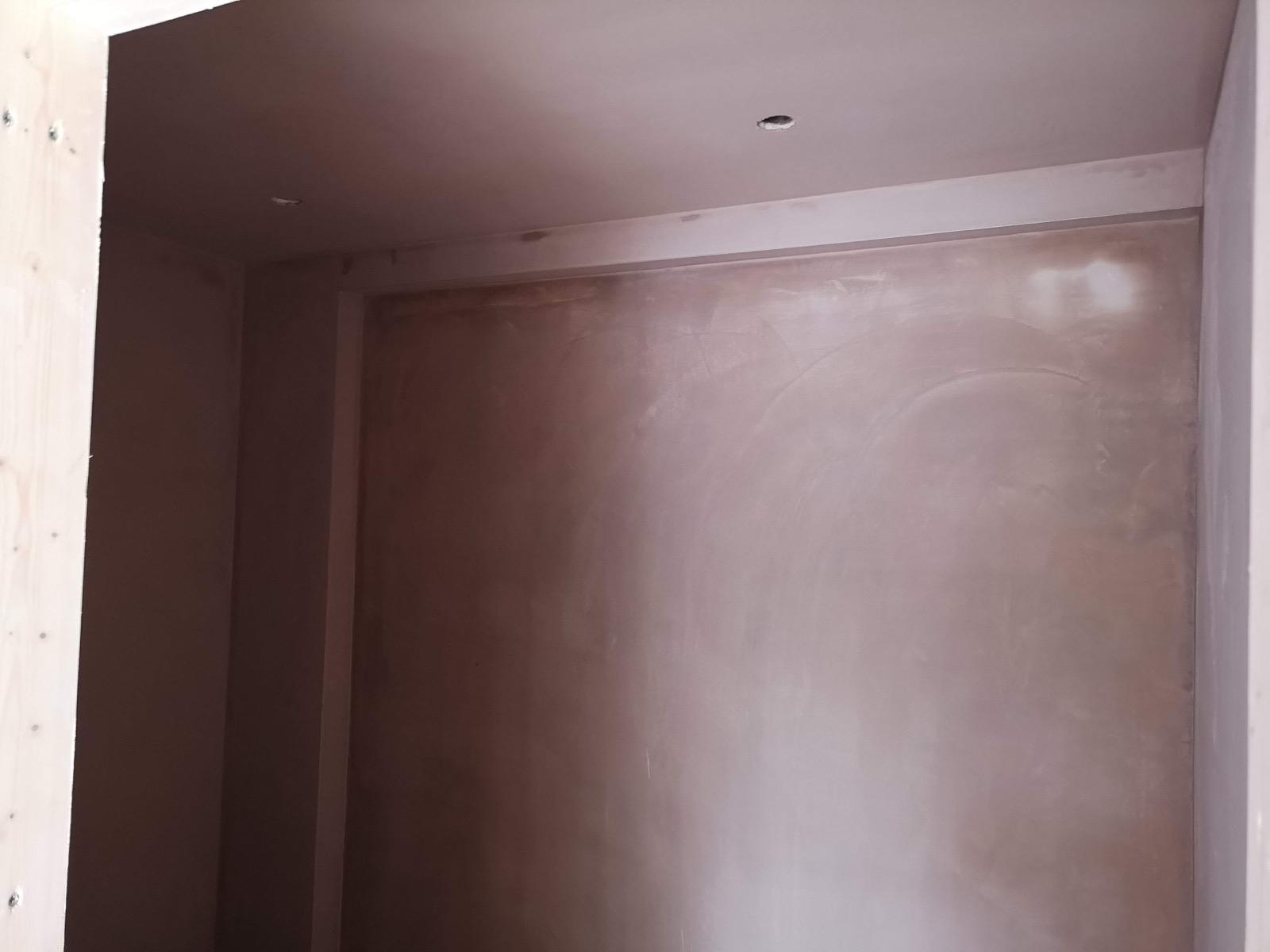 Fresh plaster across a broad interior wall beneath a ceiling with recessed spotlights