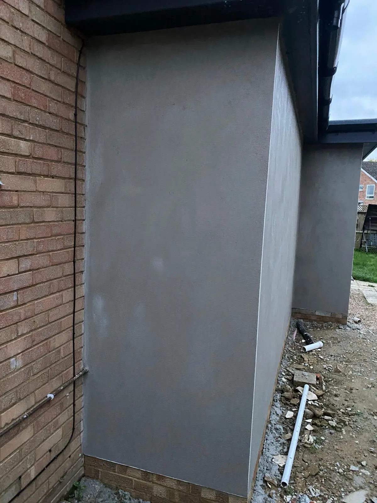 Smooth rendered extension side wall beside brickwork