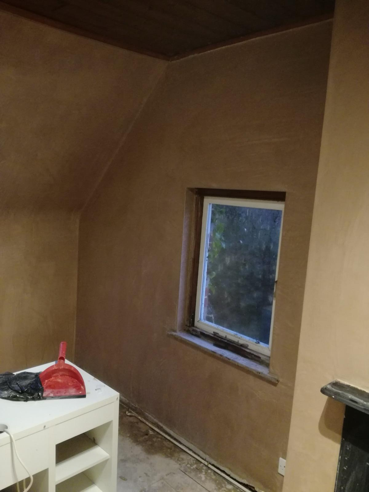 New plaster on an interior wall surrounding a window, with a table and dustpan nearby