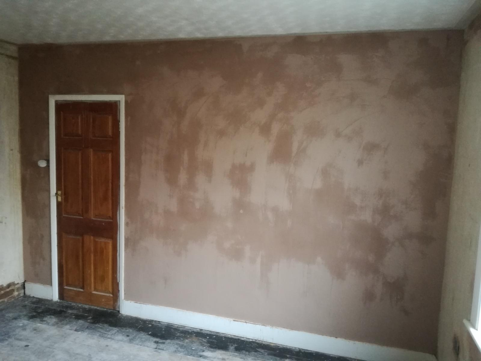 Fresh plaster drying across a large wall beside a timber door