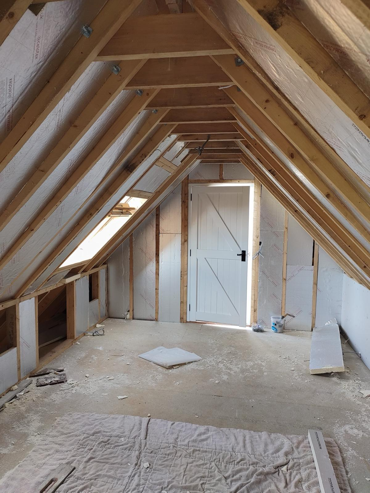 Timber-framed loft with insulation boards fitted and a white ledged door