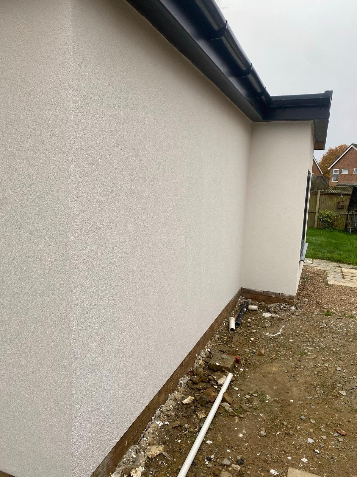 Light-coloured finished render beneath black roof trim