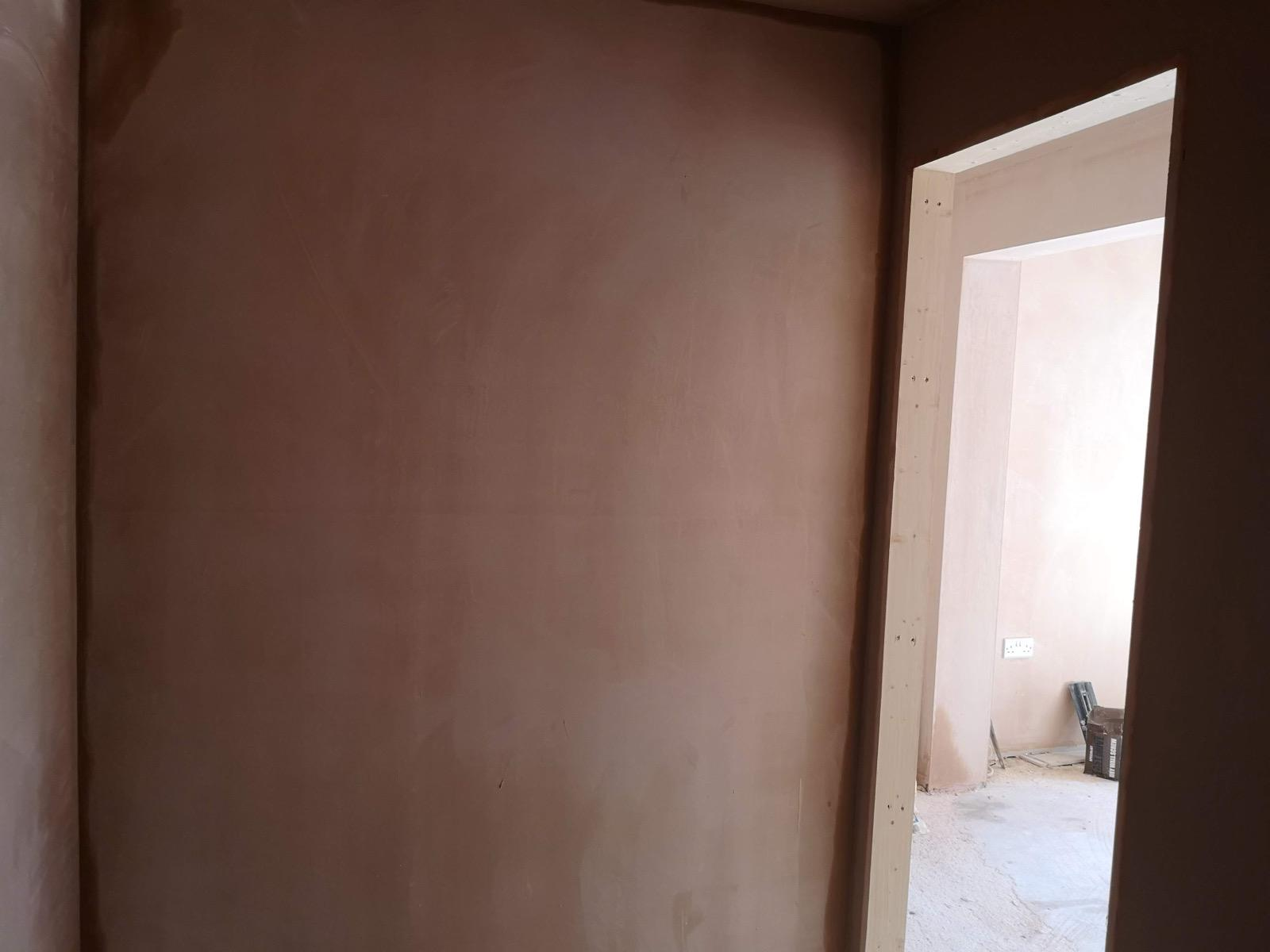 New plaster across an interior wall beside a wide timber-framed doorway