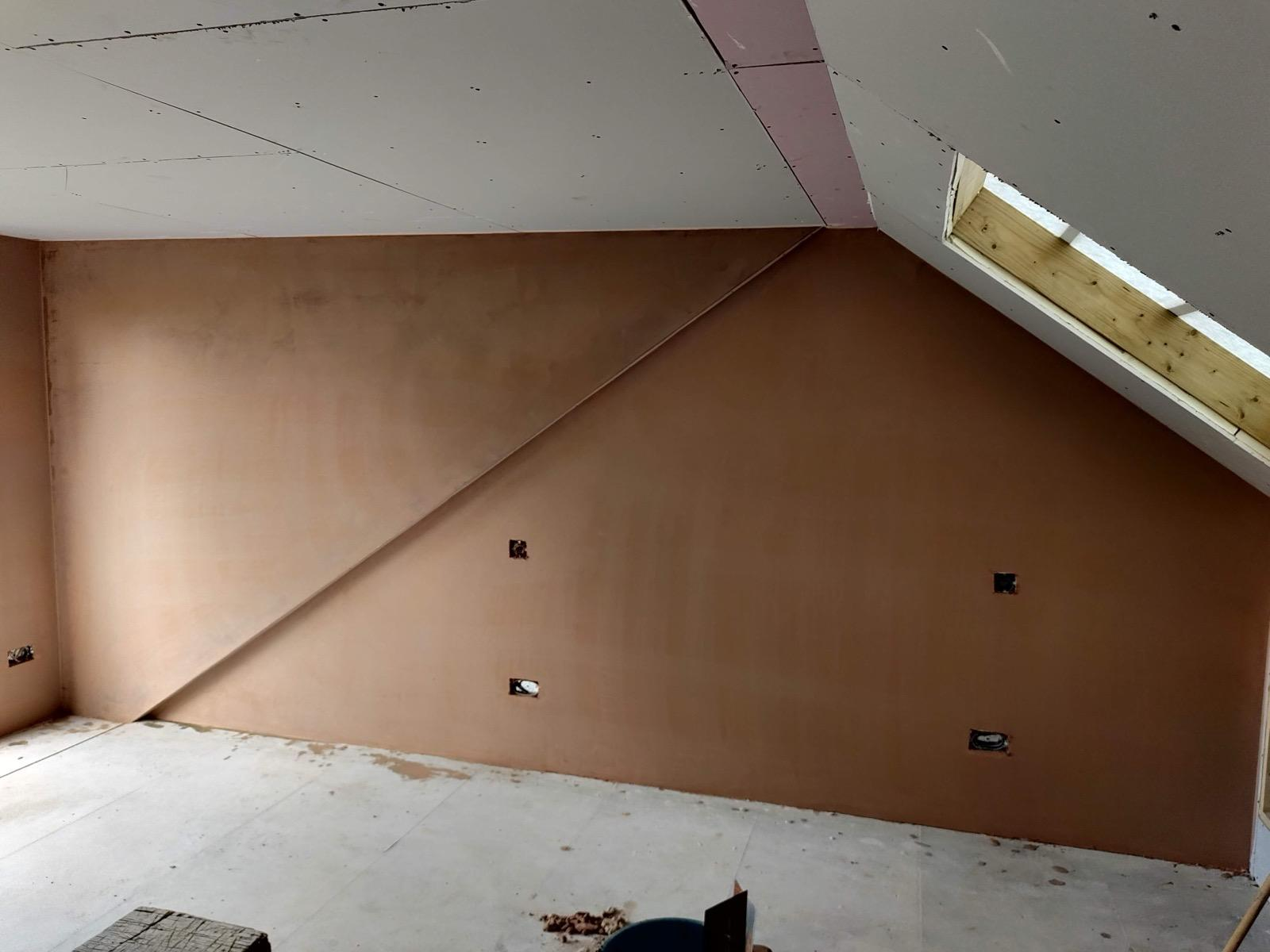 Smooth fresh plaster across a sloped loft gable wall beside a roof window