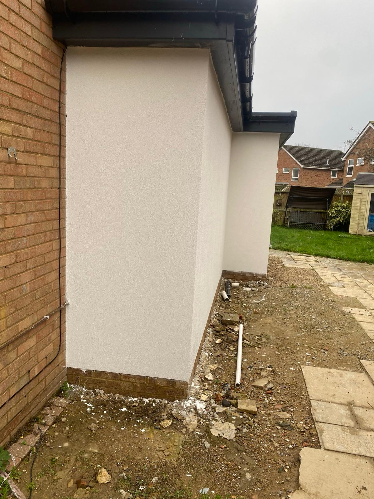 Clean light-coloured render finish on an extension side wall