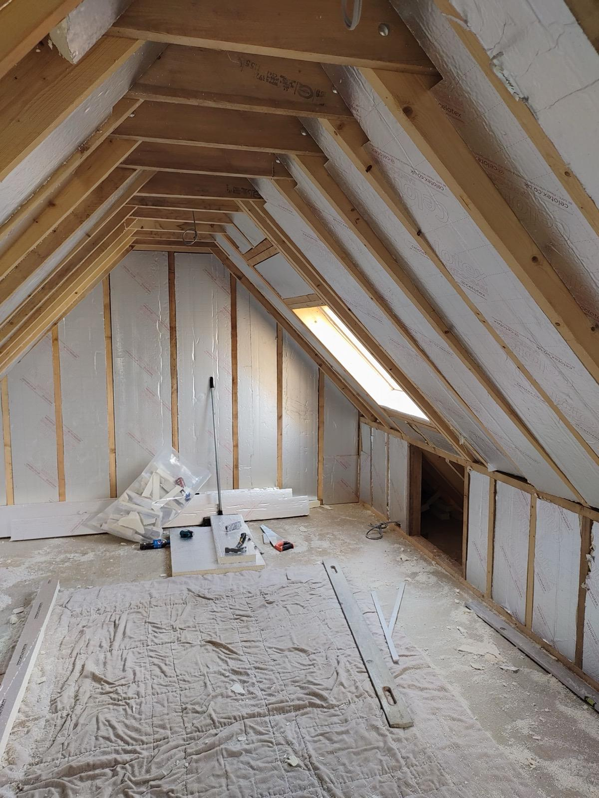 Loft room with insulation boards between rafters and a roof window