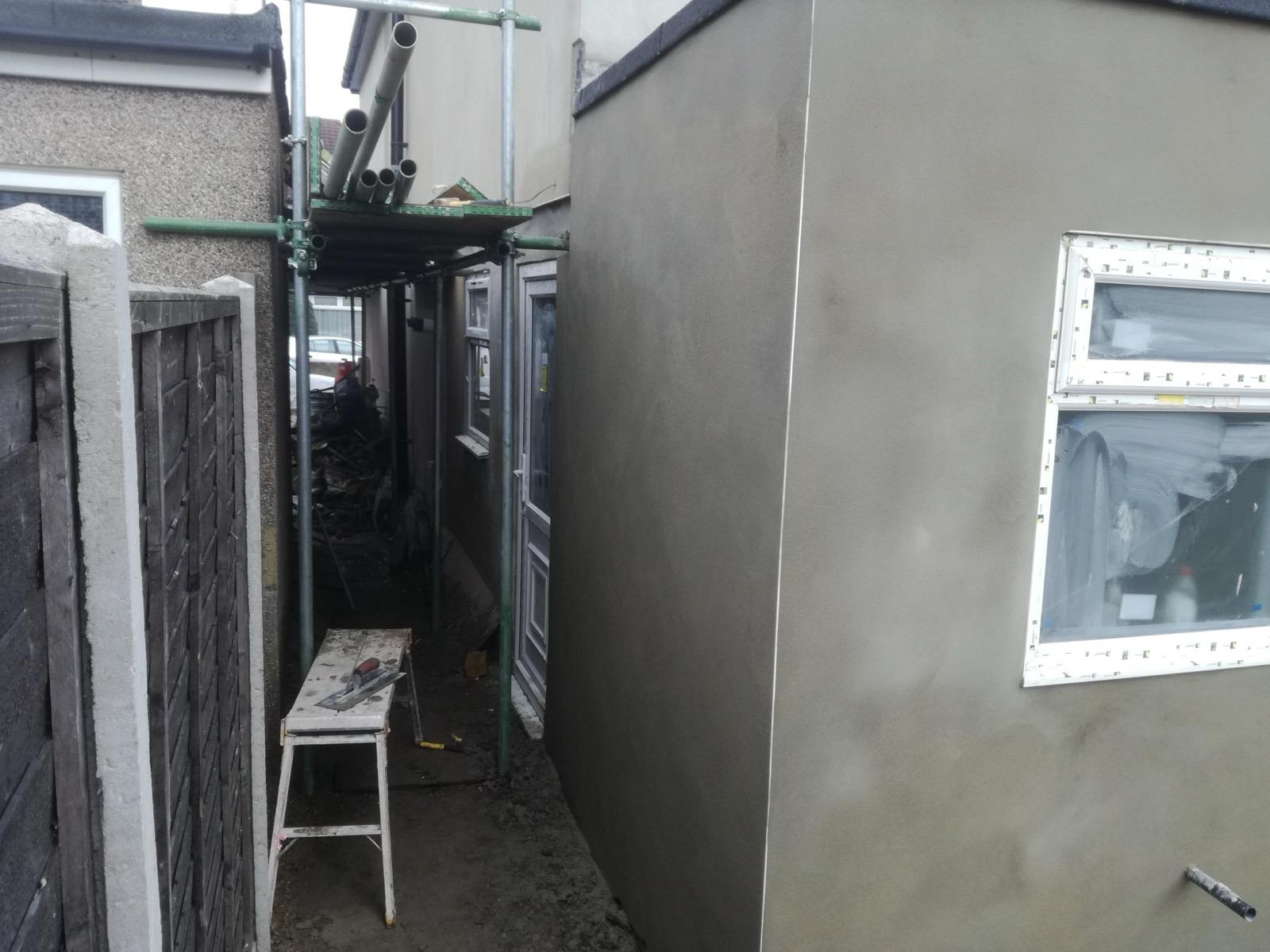 Rendered exterior side wall beside scaffolding and a narrow passage